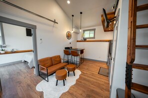 A modern living space with a sofa, ottomans, a dining area, and a kitchen counter.