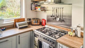 A modern kitchen with a gas stove, a toaster, and a window overlooking a garden. - 5 bedroom accommodation in Brodick, Isle of Arran (Brodick, Isle of Arran)