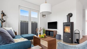 A modern living room with a sofa, coffee table, TV, and a wood-burning stove.