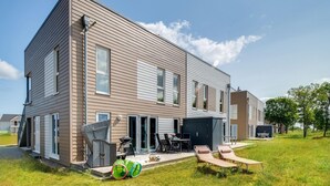 A modern two-story house with a covered patio, outdoor seating, and a garage.