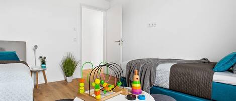 A modern, well-lit bedroom with a bed, a small round table with toys, a potted plant, and a blue sofa.