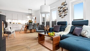 A modern living room with a blue sofa, a wooden coffee table, and a dining area with a white table and chairs.