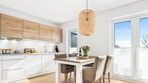 A modern kitchen with white cabinets, a wooden dining table, and a large window.