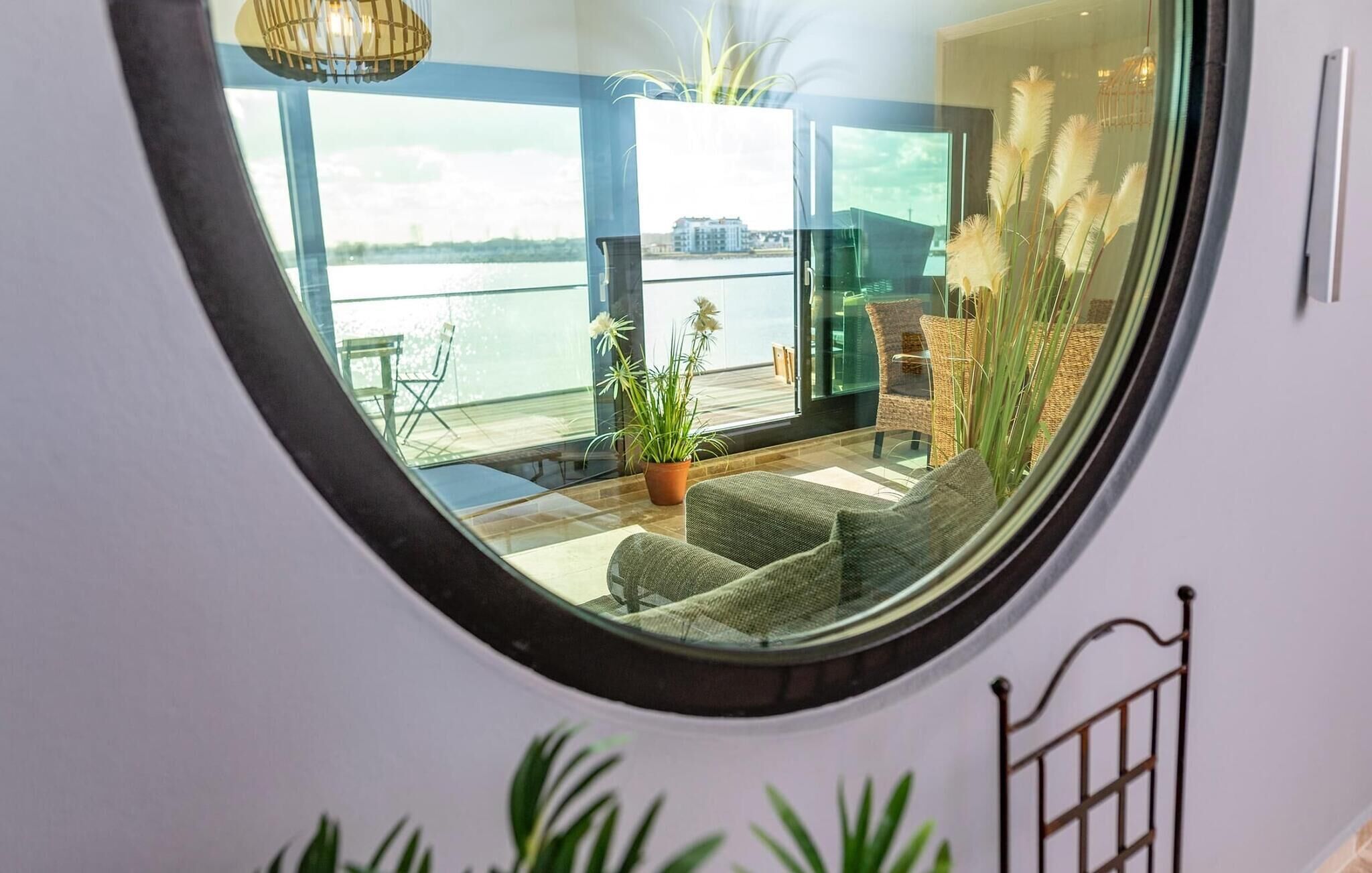 A circular window with a view of a balcony area featuring wicker furniture, a potted plant, and a view of a body of water.
