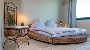 A room with a bed, a small table, a lamp, and a decorative wall piece.
