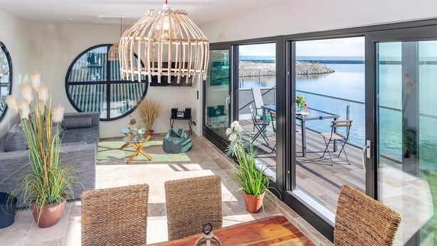 A modern living room with a large glass door leading to a balcony with a view of the sea.