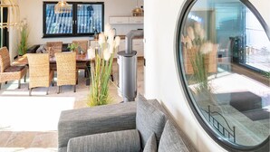 A modern living room with a grey sofa, wicker chairs, a dining table, and a large window with a view of the street.