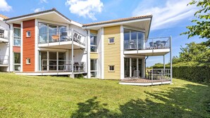 A modern two-story house with a balcony on the upper floor, a deck area, and a well-maintained lawn. - Gudhjem Søpark Lejl. 25 (Gudhjem)