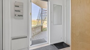 A room with a door leading outside, a window with a view of a staircase, and a wall-mounted electrical panel. - Gudhjem Søpark Lejl. 25 (Gudhjem)