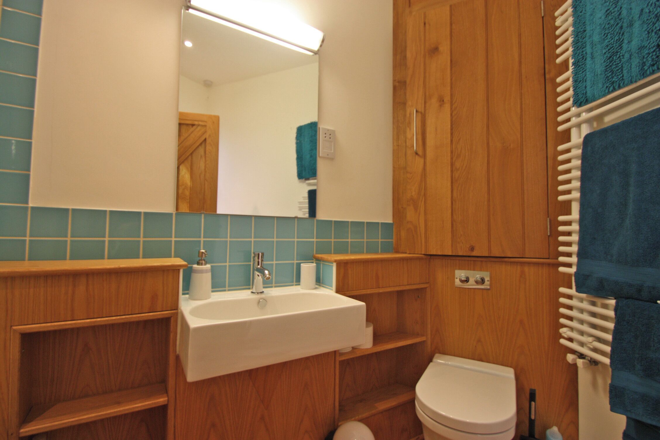 A bathroom with a wooden vanity, a white sink, a mirror, a toilet, and a towel rack.