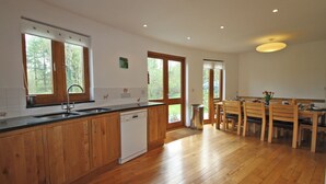 A kitchen with wooden cabinets, a dishwasher, and a dining area with wooden chairs and a table. - 4 bedroom accommodation in Cilycwm, Llandovery (Cilycwm, Llandovery)