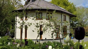A round building with multiple windows and a sloped roof, surrounded by a garden with various plants and flowers. - 4 bedroom accommodation in Cilycwm, Llandovery (Cilycwm, Llandovery)