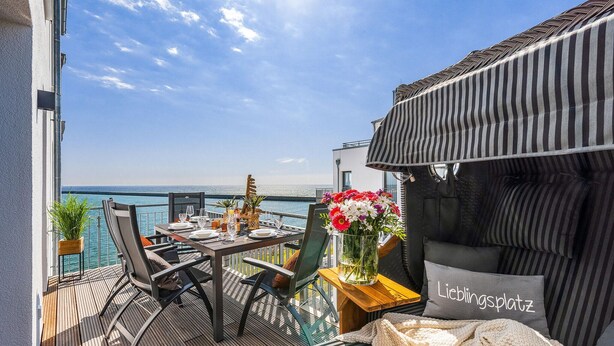 A balcony with a table set for dining, a sofa, and a view of the sea.