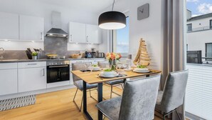 A modern kitchen with white cabinets, a black stove, and a dining area with a wooden table and grey chairs.