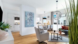 A modern living room with a grey armchair, a round coffee table, and a dining area with a large painting.