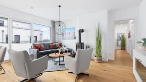 A modern living room with a sofa, chairs, a coffee table, a fireplace, and large windows.