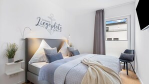 A modern bedroom with a bed, bedside tables, a desk, and a window with a view.