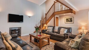 Un salon avec une cheminée, des canapés en cuir, une table basse en bois, un escalier et un téléviseur fixé au mur.