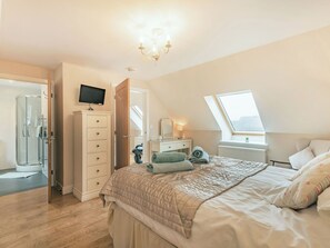 Une chambre à coucher comprenant un lit, une commode, un téléviseur, une fenêtre et un puits de lumière.