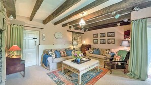 A cozy living room with exposed wooden beams, a sofa set, a patterned rug, and a small table with a vase.