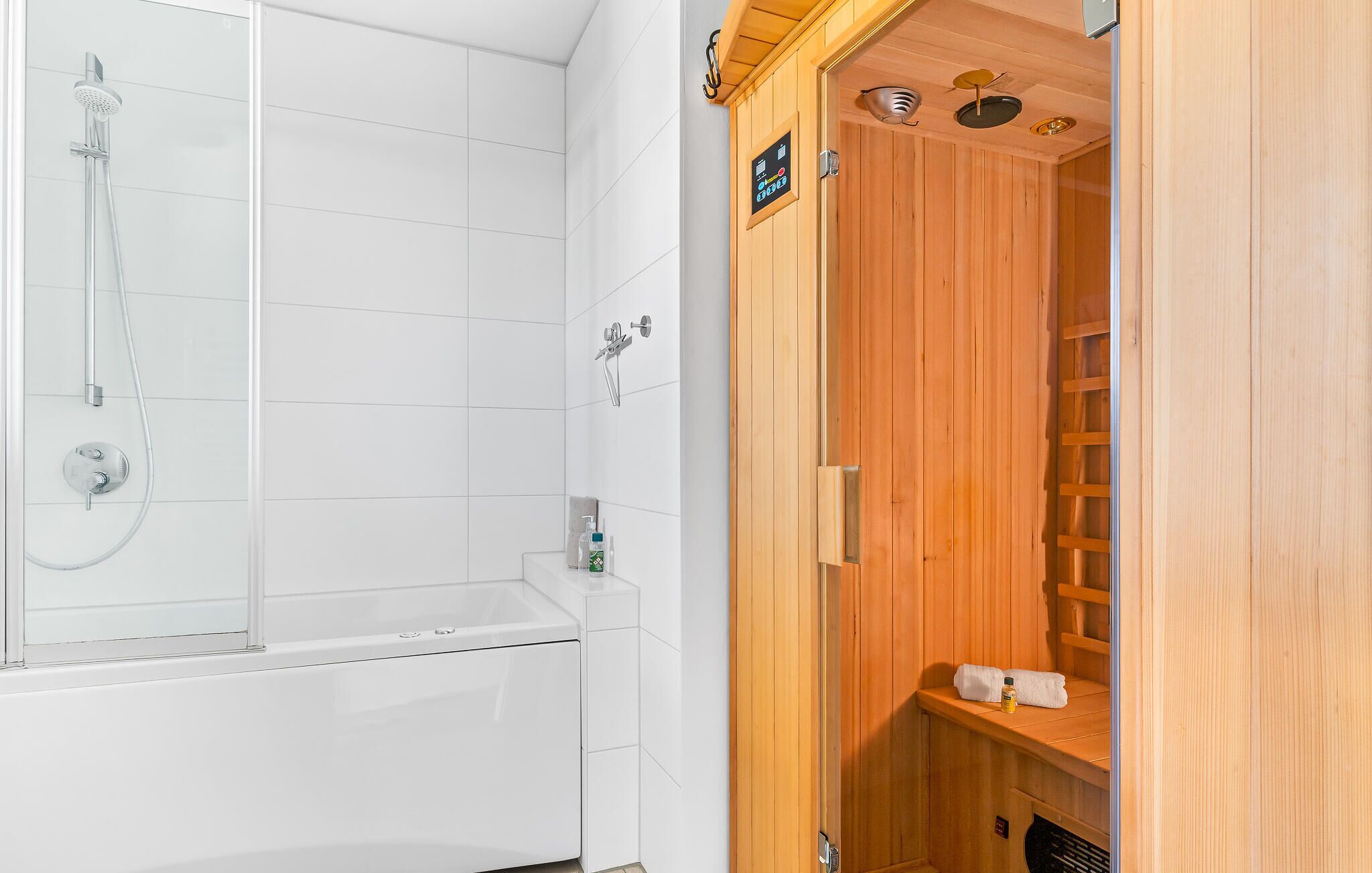 A modern bathroom with a glass-enclosed shower, a wooden sauna, and a white tiled wall.