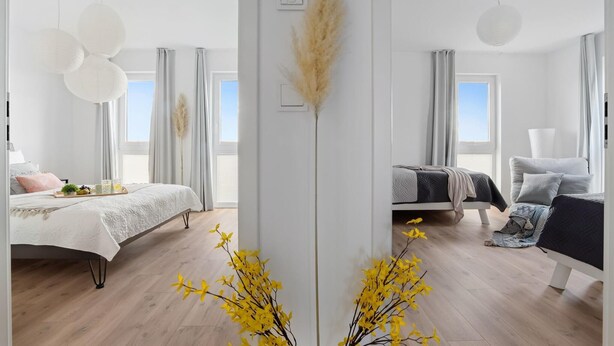 Ein modernes Schlafzimmer mit einem großen Bett, einem Einzelbett und einer Schlafcouch. Es gibt Fenster mit Vorhängen, einen Nachttisch mit Lampe sowie ein Tablett mit Früchten und Getränken auf dem Bett.