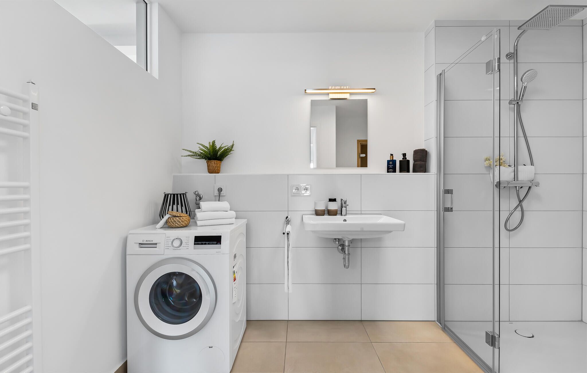 Een moderne badkamer met een wasmachine, wastafel en douche.