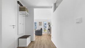 A modern, minimalist hallway with a wooden floor, white walls, and a grey sofa in the background.