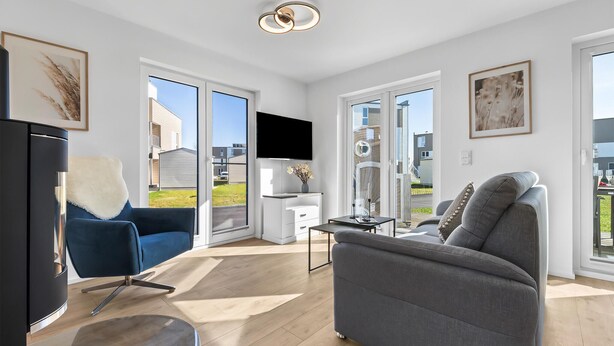 A modern living room with a grey sofa, a blue armchair, and a flat-screen TV mounted on the wall.