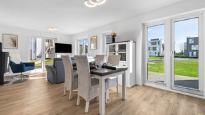 A modern living room with a dining area, large windows, and a view of the outside.