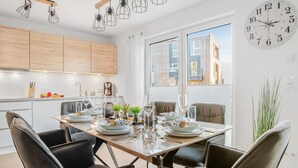 Une cuisine moderne avec des meubles en bois, une table à manger pour six personnes et une grande fenêtre donnant sur des immeubles.