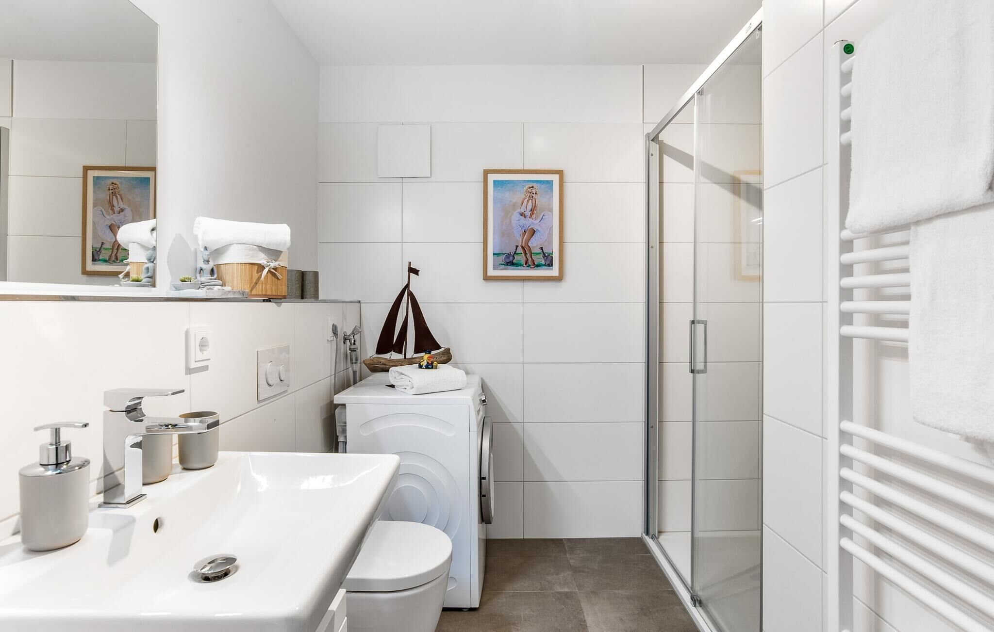 A modern bathroom with a sink, toilet, and washing machine. There are framed pictures on the wall and a towel rack.