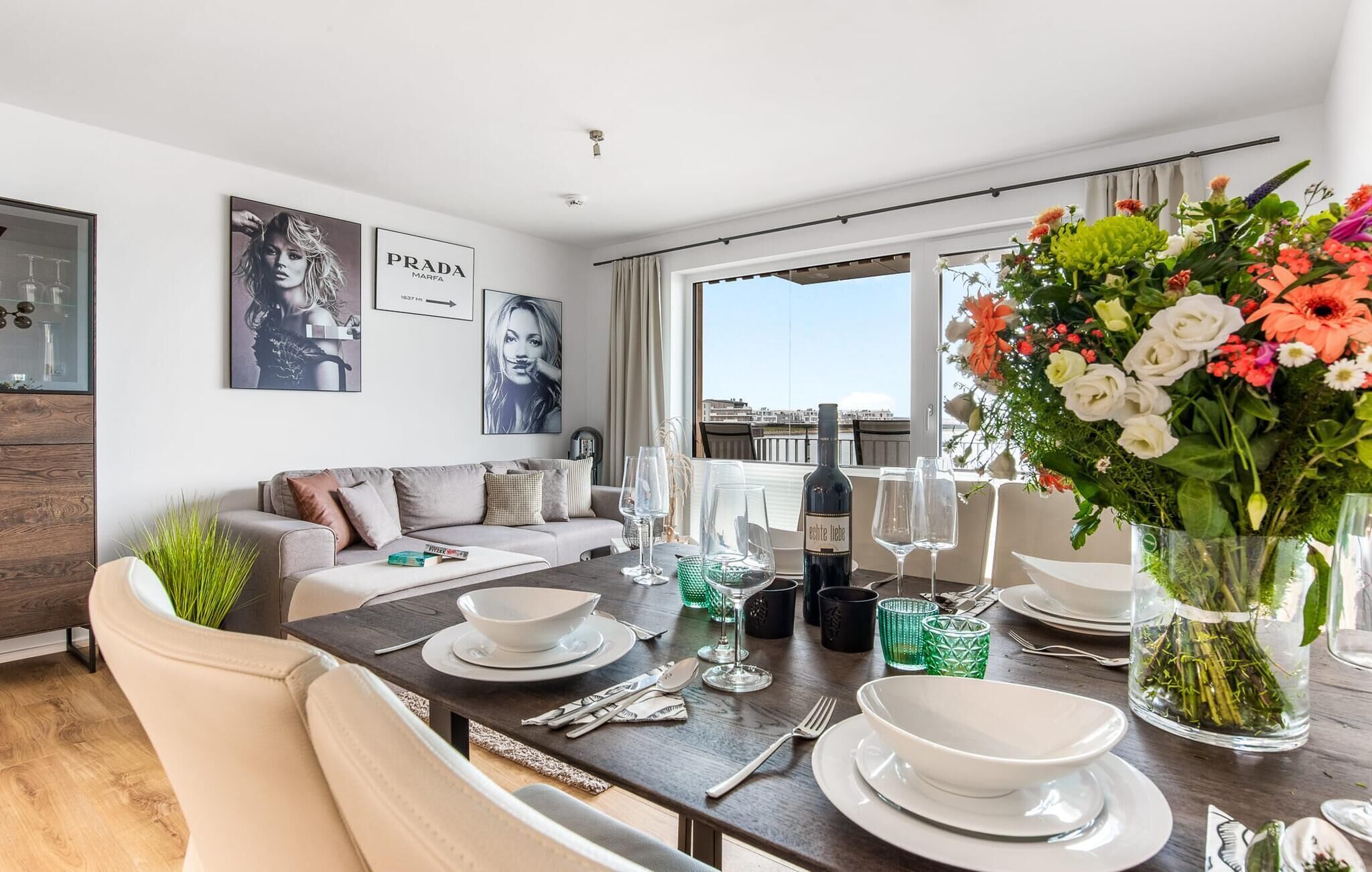 A modern dining area with a table set for two, a sofa, and a view of the city.