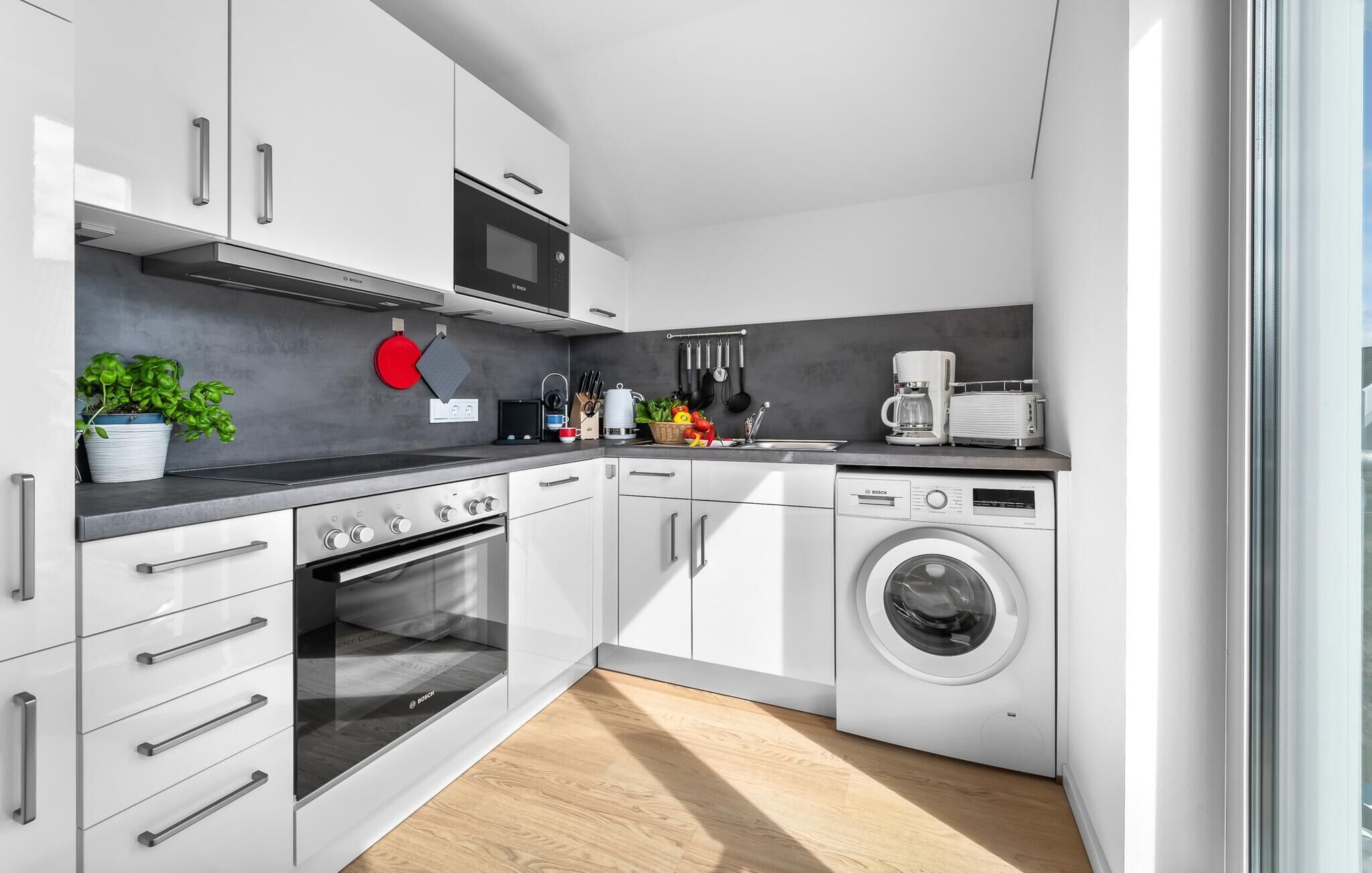 Une cuisine moderne avec des armoires blanches, un four à micro-ondes Bosch, un four encastré, un lave-linge Bosch et une machine à café.