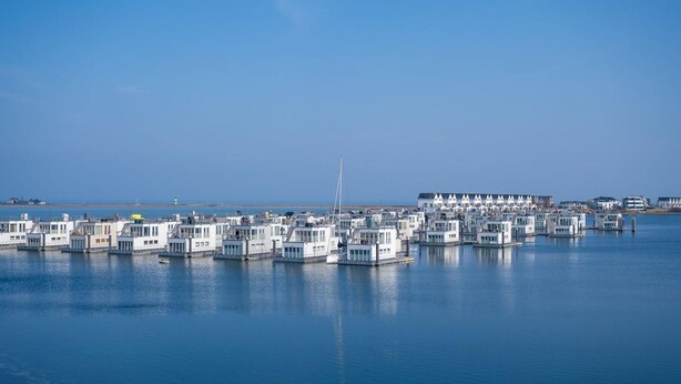 A marina with numerous floating buildings, a clear sky, and a distant lighthouse.