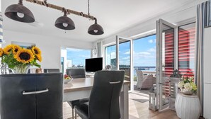 A modern living room with a dining area, large windows, and a view of the sea.