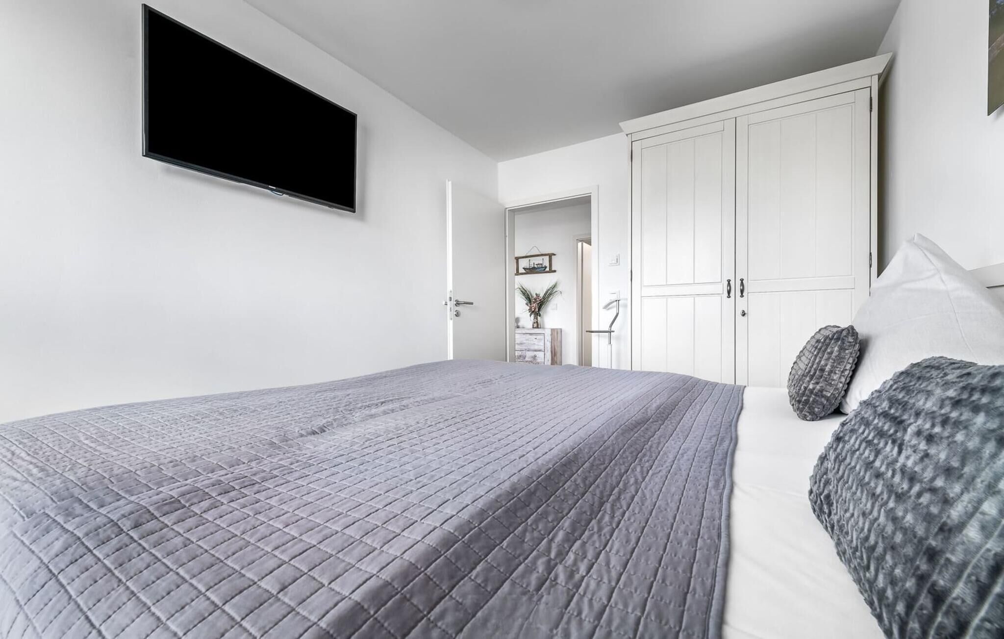 A bedroom with a bed, a wardrobe, and a television mounted on the wall.