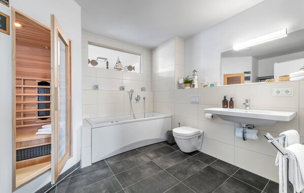 Ein modernes Badezimmer mit Badewanne, Toilette und Waschbecken. Eine Holzregaleinrichtung beherbergt Handtücher und Toilettenartikel.