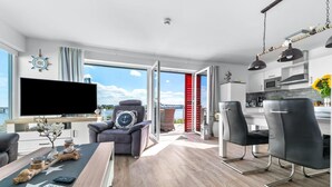 A modern living room with a flat-screen TV, a dining area with a wooden table, and a kitchen with a microwave.