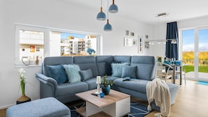 En moderne stue med en grå sofa, et træbord og udsigt til en balkon med bybillede.