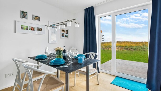 Et spiseområde med et bord dækket til to, et stort vindue med udsigt over et mark og billeder i rammer på væggen.
