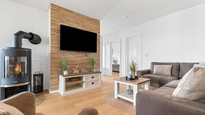 Un soggiorno moderno con stufa a legna, televisore a schermo piatto montato su una parete in legno, un divano grigio e un tavolino da caffè.