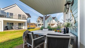 Una veranda coperta con tavolo e sedie, un barbecue e vista sulle case vicine.