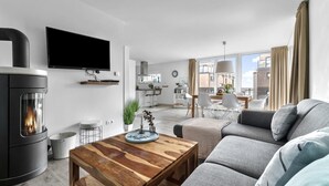A modern living room with a fireplace, a flat-screen TV, a dining area with a table and chairs, and a view of the city through large windows.