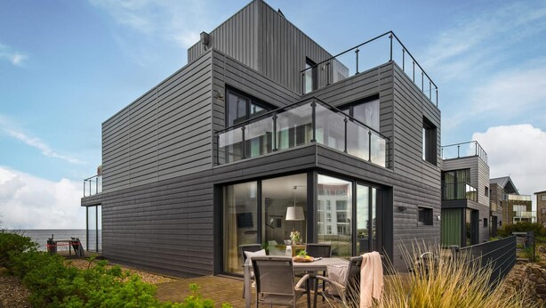 A modern two-story house with a flat roof, large windows, and a balcony.