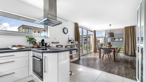 A modern kitchen with a built-in oven and stove, a dining area with a table and chairs, and a large sliding glass door leading to a balcony.