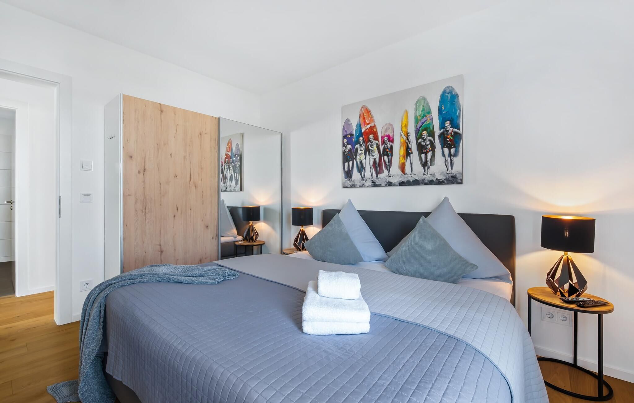 Une chambre à coucher moderne avec un grand lit, une armoire en bois, un tableau au mur et une table de chevet avec une lampe.