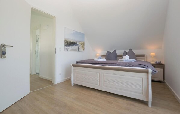 A bedroom with a bed, a nightstand, a lamp, a painting, and a door leading to a bathroom.