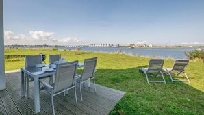 An outdoor dining area with a table and chairs, overlooking a body of water with buildings in the background.