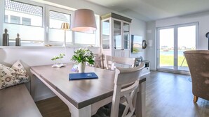A modern kitchen with white cabinetry, a dining table with chairs, and a view of the outdoors through large windows.